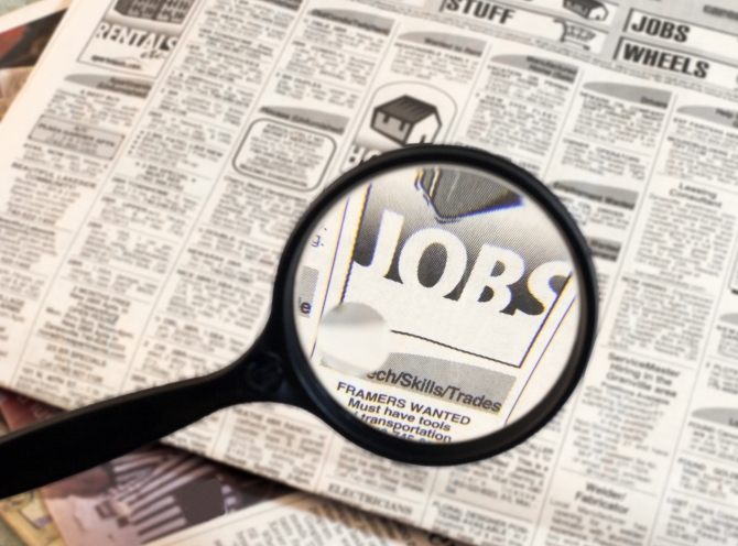 newspaper opened to the want ads.  magnifying glass highlighting the word jobs.