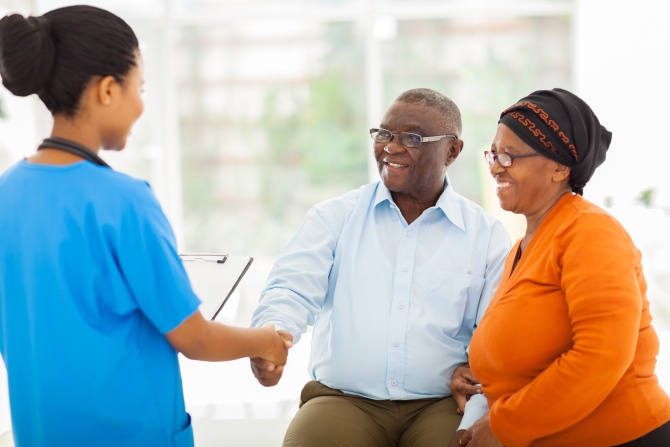 friendly african female nurse greeting senior couple in hospital