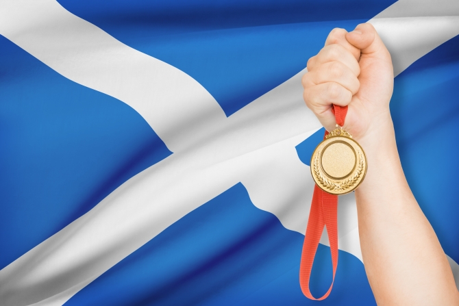 Sportsman holding gold medal with flag on background - Scotland