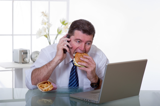 man at office with phone eat unhealthy fast food
