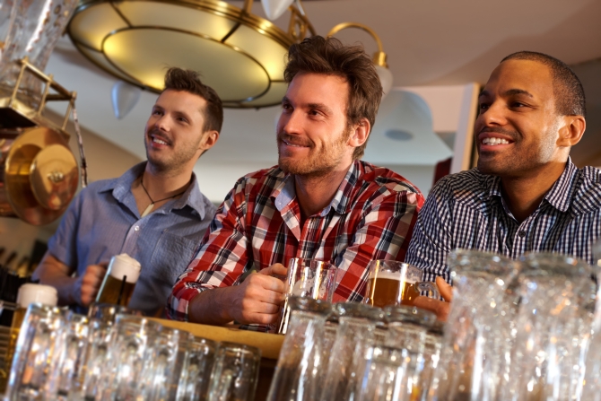 Portrait of young men drinking beer at bar counter, smiling.